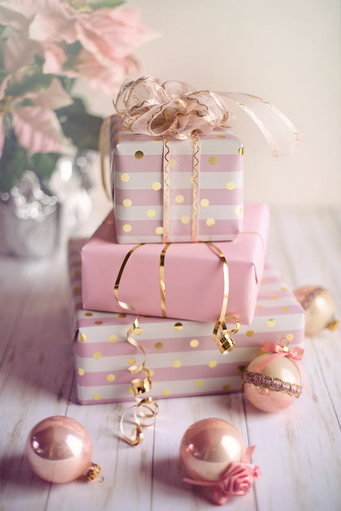 Charming Christmas presents wrapped in pink and gold with festive ornaments on a wooden table.